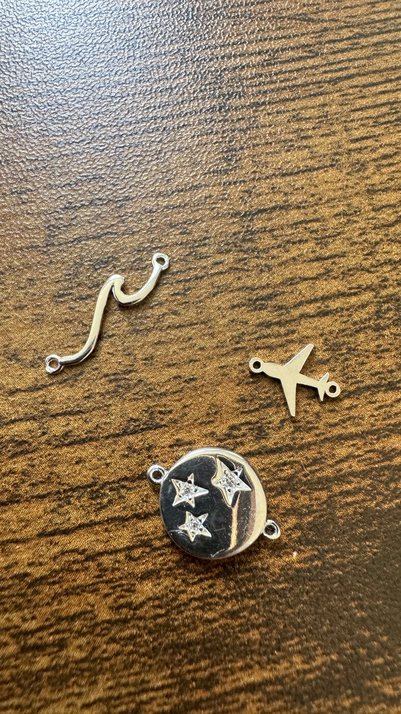 Small gold charms — swoosh, airplane, and star disc — on a wooden surface